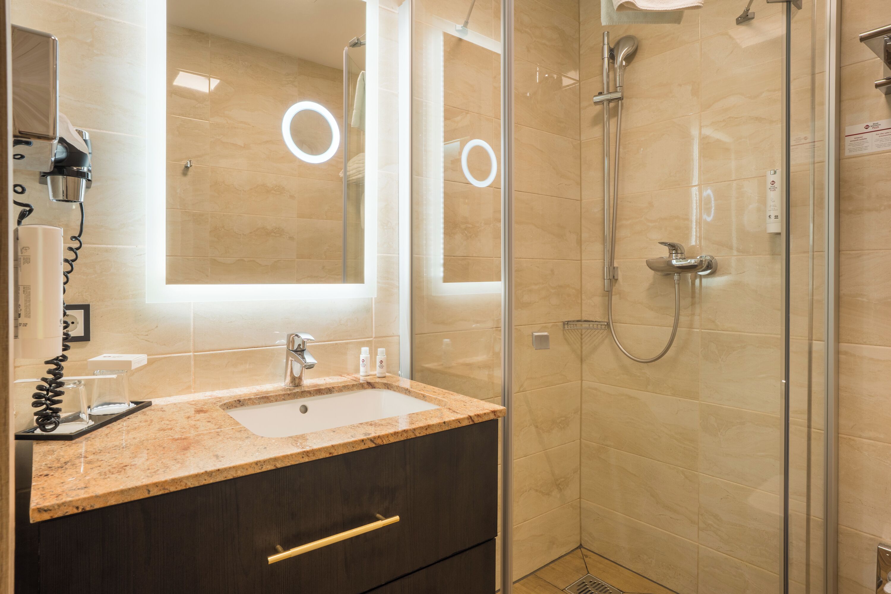 Un baño moderno con encimera de granito, lavabo, espejo y ducha con paredes de vidrio.