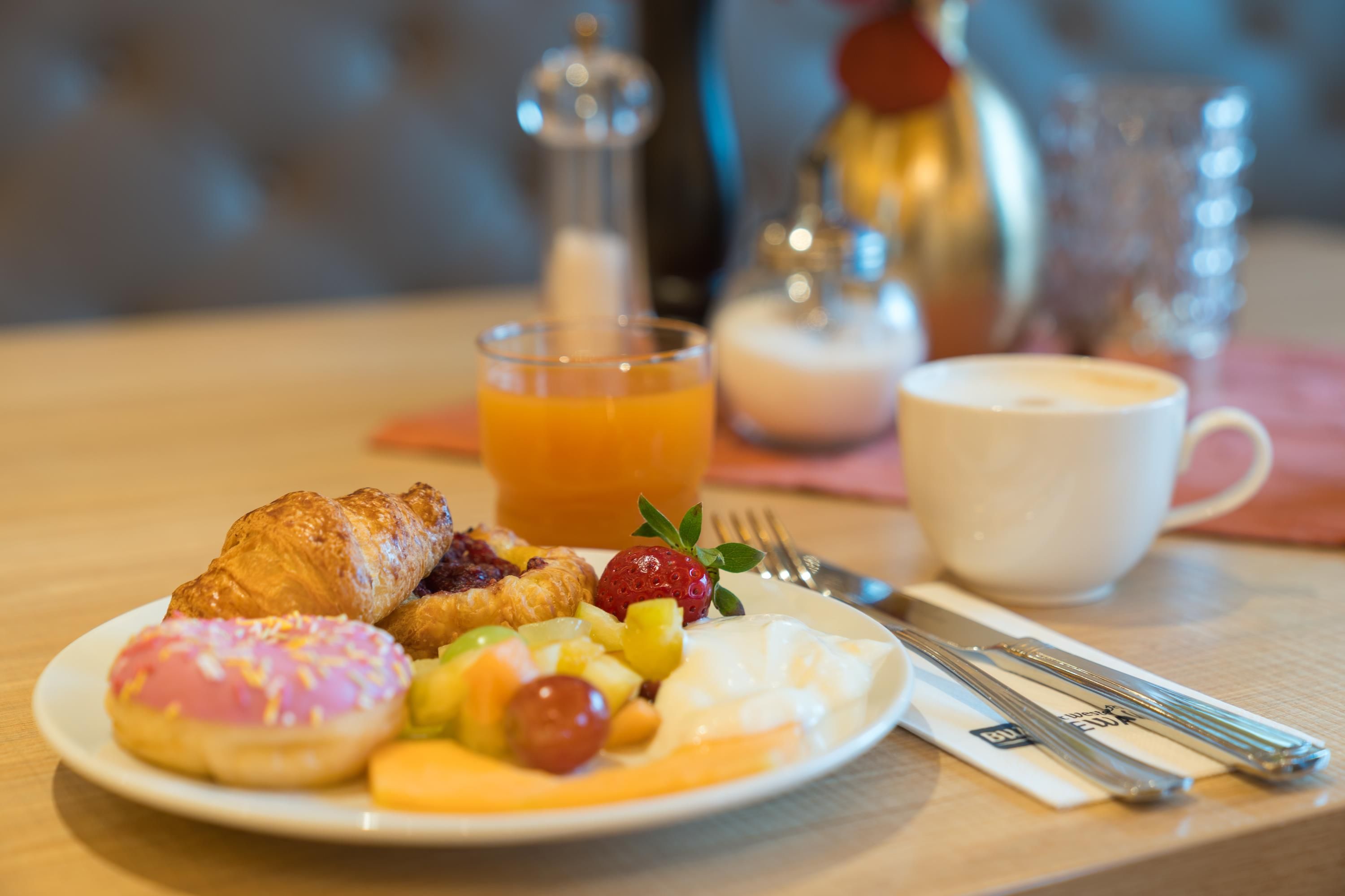 A breakfast setting with a croissant, fruit, and a cup of coffee on a table.