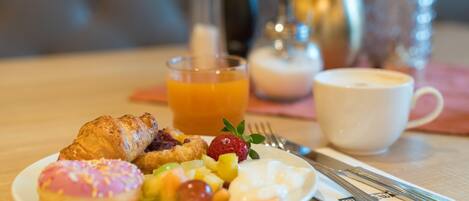 Mesa posta para o café da manhã com um croissant, frutas e uma xícara de café.