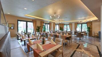A spacious dining area with multiple tables and chairs, large windows, and ceiling lights.