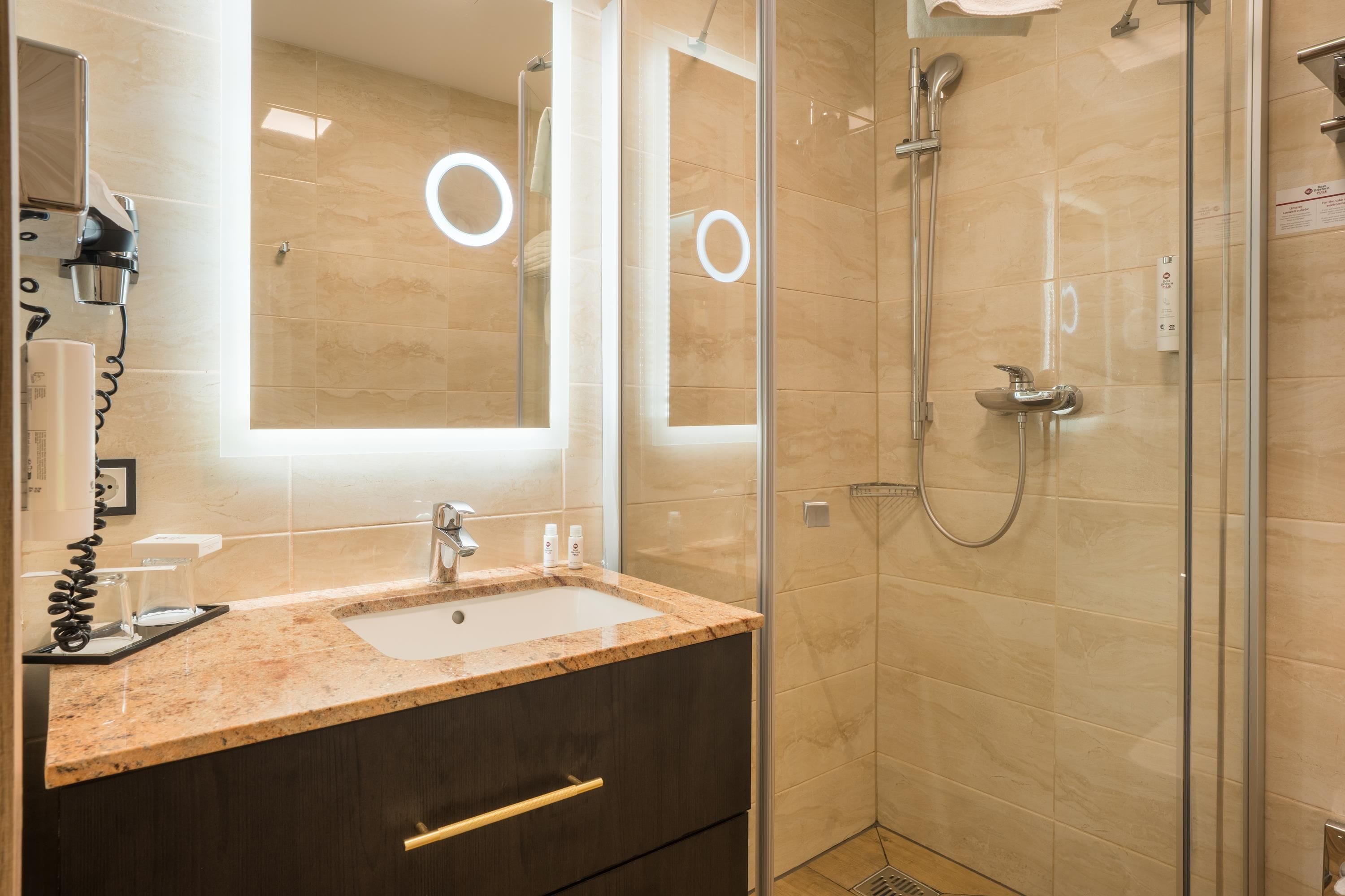 A bathroom with a marble sink, a mirror, a handheld showerhead, and a glass-enclosed shower.