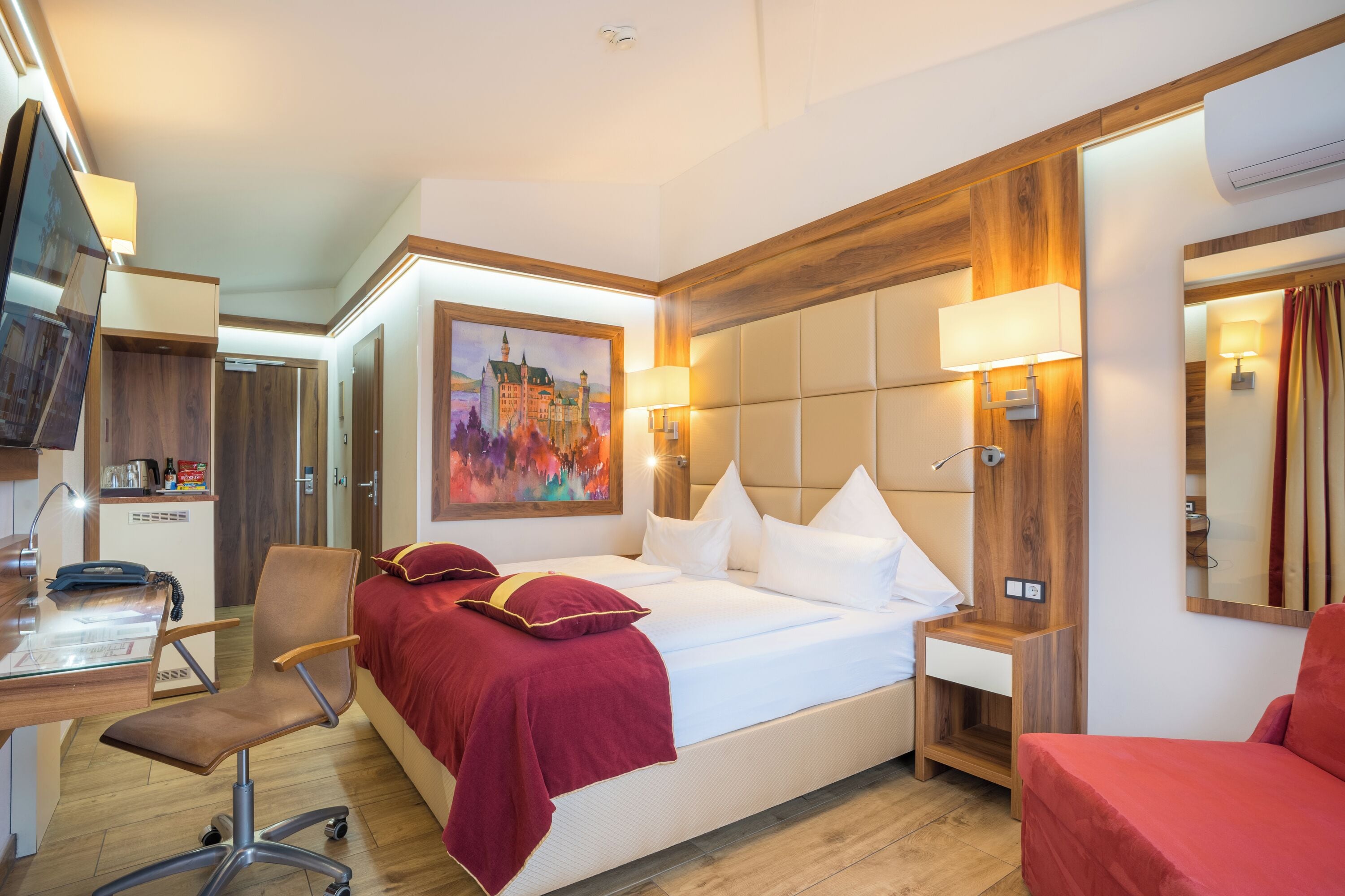 A hotel room with a bed, desk, chair, and a painting on the wall.