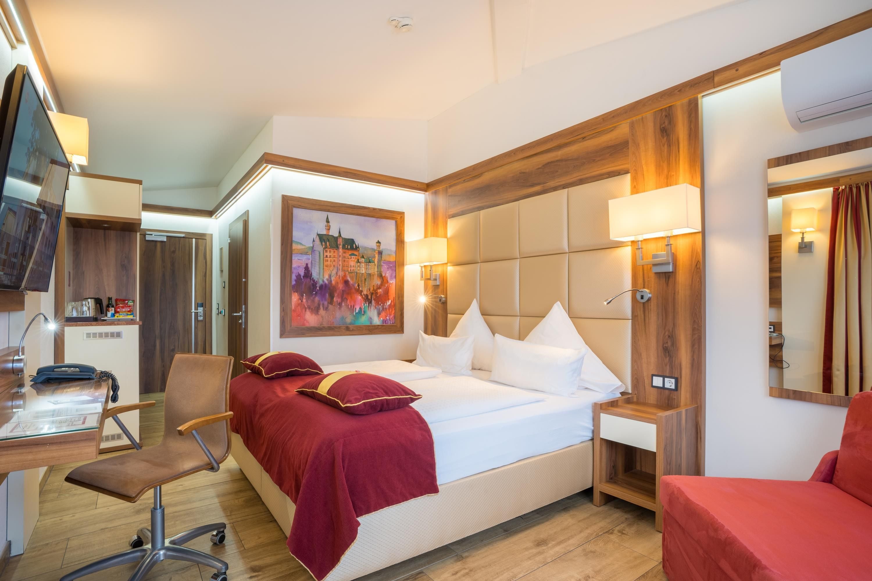 Una habitación de hotel con cama, escritorio, silla, un cuadro y un espejo.