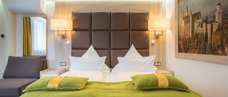 Een hotelkamer met een groot bed, twee nachtkastjes, een slaapbank en een schilderij aan de muur.