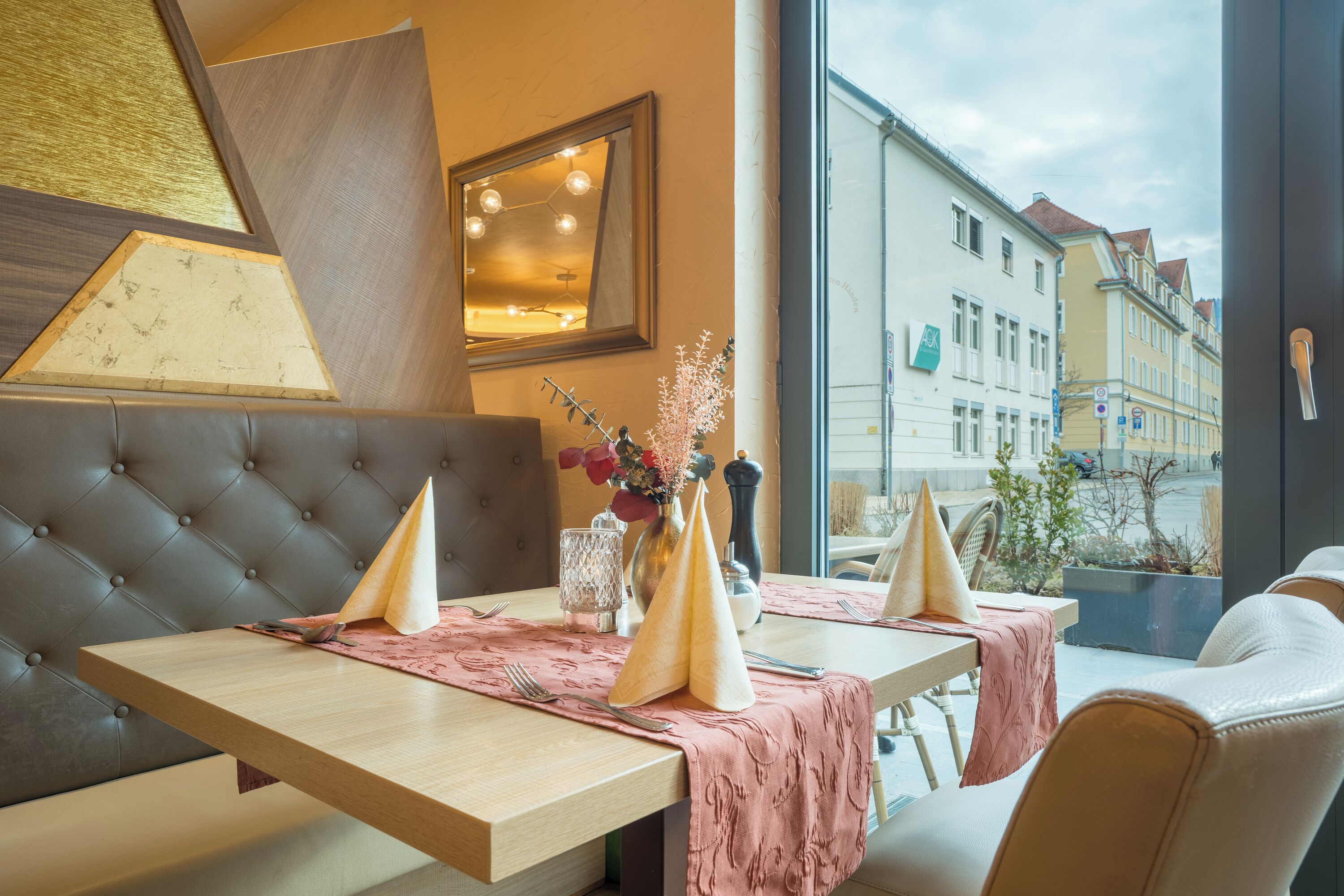 A dining area with a wooden table, cushioned seating, and a view of buildings through a window.