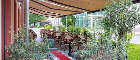 An outdoor seating area with tables and chairs, a covered walkway, and a building in the background.