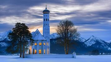 A church with a tall bell tower and a snow-covered landscape with mountains in the background.