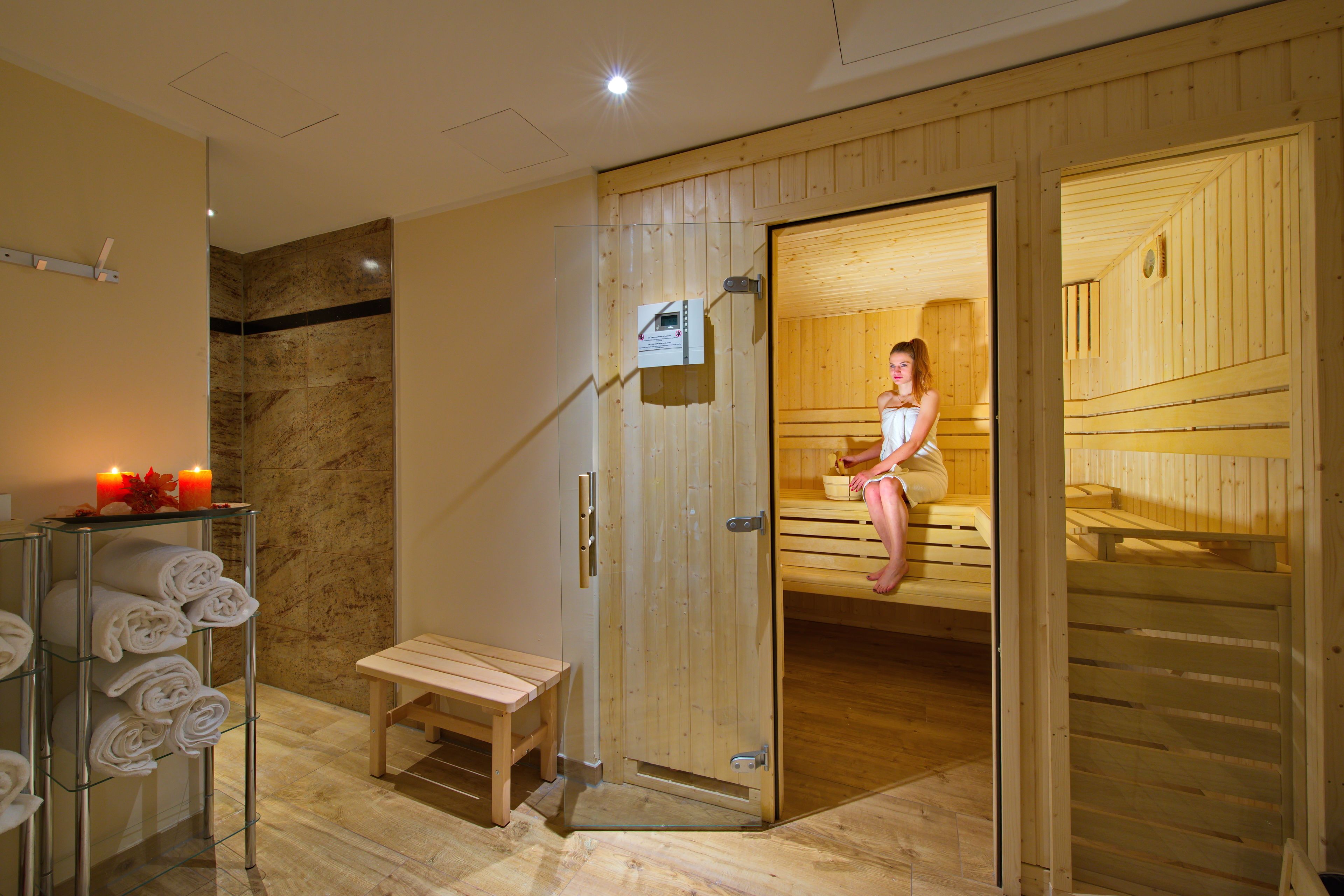 Un cuarto de sauna con bancos de madera y un banco afuera. Hay un perchero con toallas y una vela sobre una repisa.