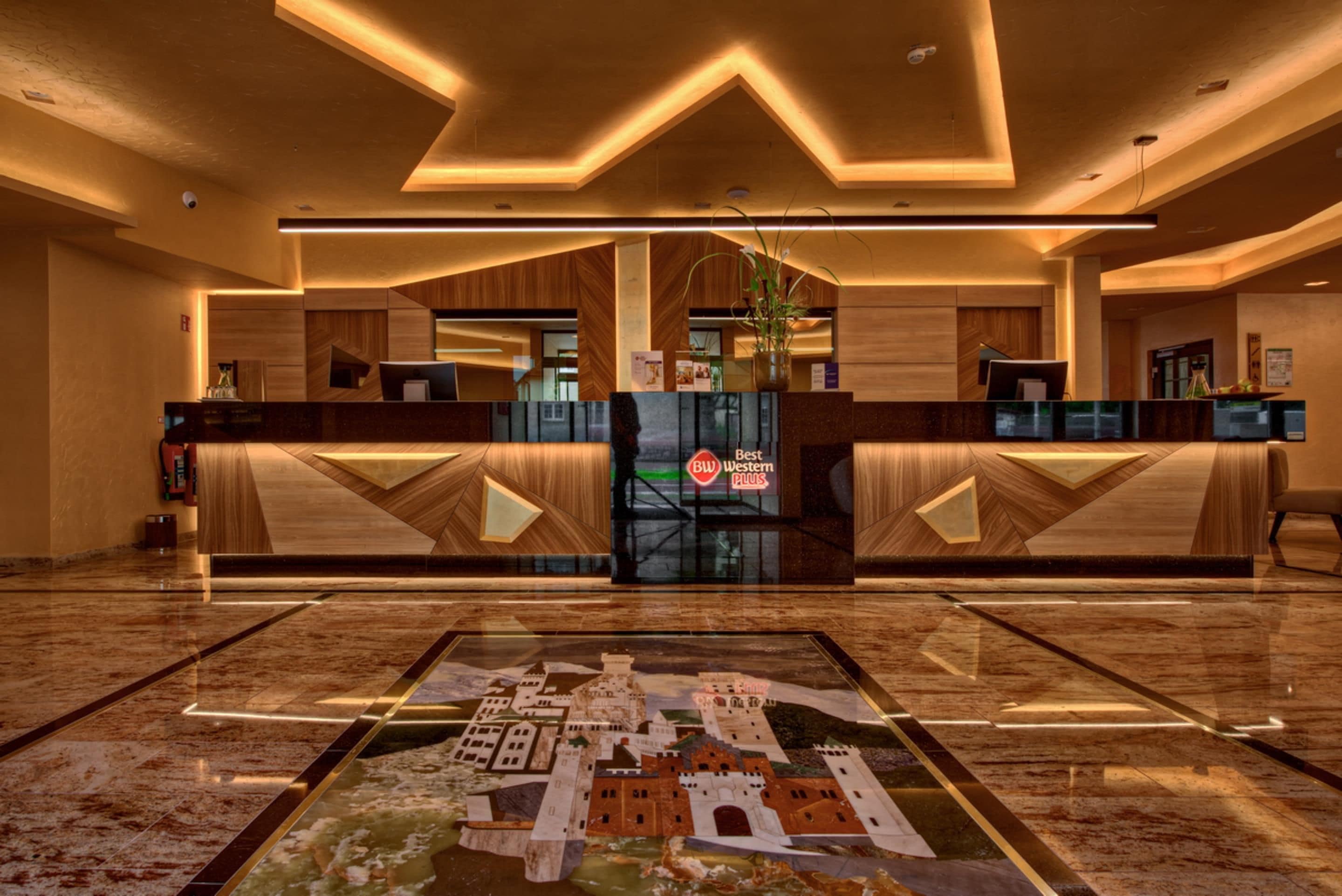 Un vestíbulo de hotel con una recepción, una alfombra decorativa grande y un diseño de techo moderno.