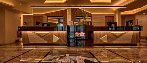 Un vestíbulo de hotel con una recepción, una alfombra decorativa grande y un diseño de techo moderno.