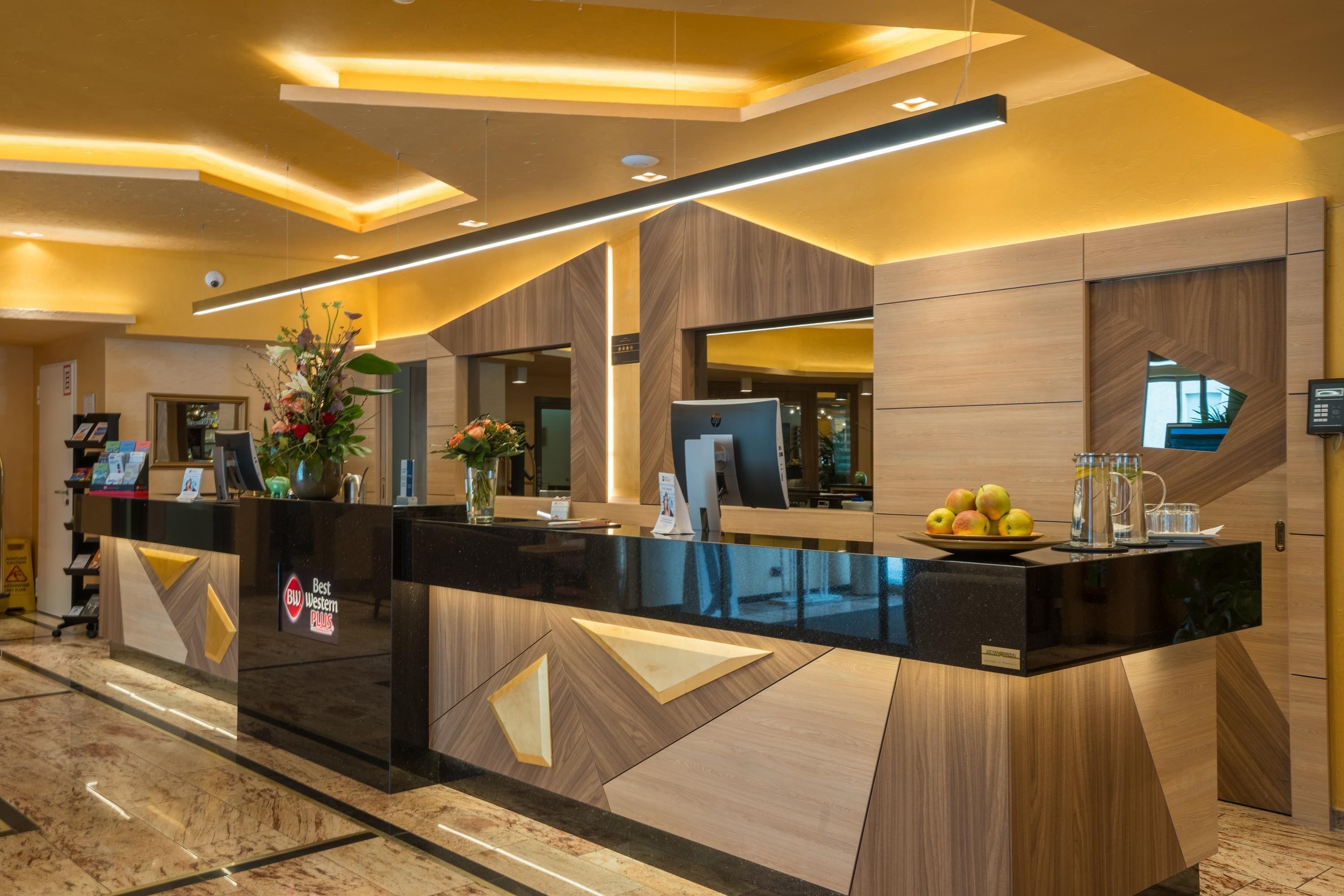 Una recepción de hotel con diseño moderno, que presenta una encimera negra, detalles de madera y un jarrón con flores.