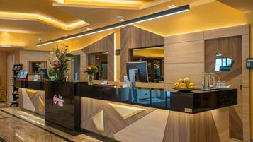 Una recepción de hotel con diseño moderno, que presenta una encimera negra, detalles de madera y un jarrón con flores.