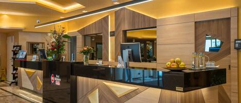 Una recepción de hotel con diseño moderno, que presenta una encimera negra, detalles de madera y un jarrón con flores.
