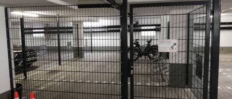 A gated parking area with a metal fence, a sign indicating bicycle parking, and a pair of traffic cones.