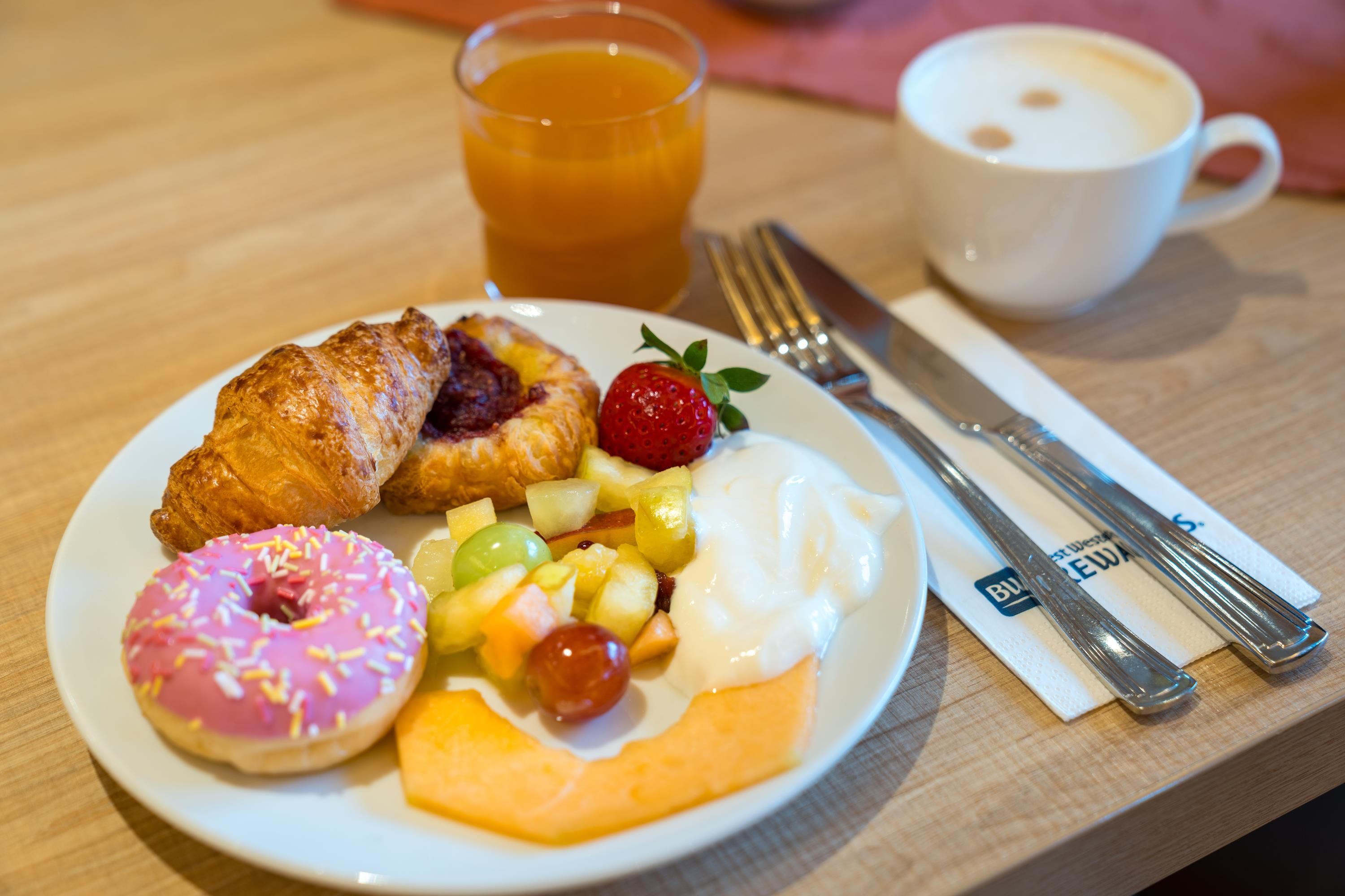 Un plato de desayuno con croissant, dona, fruta y yogur.