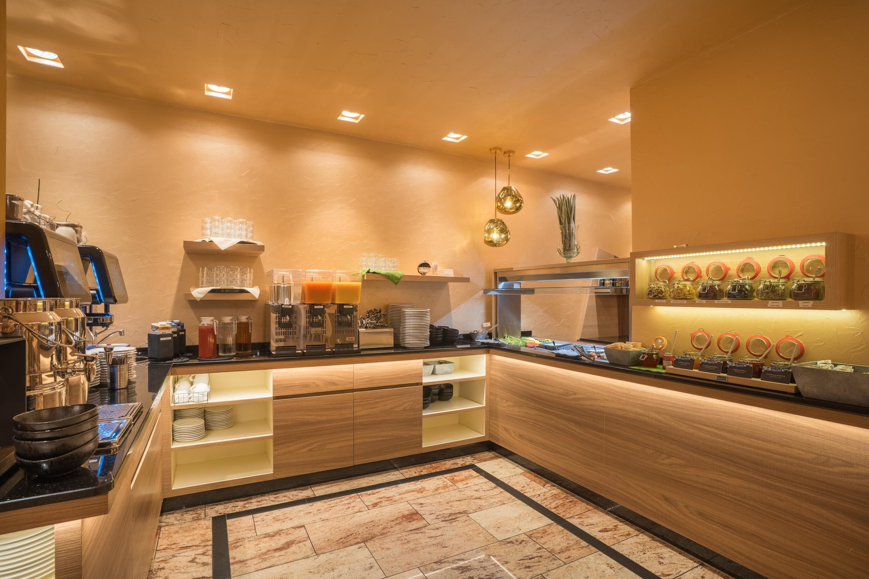 A modern kitchen with a central island, equipped with a coffee machine, tea station, and various food items.