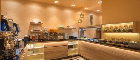 A modern kitchen with a central island, equipped with a coffee machine, tea station, and various food items.