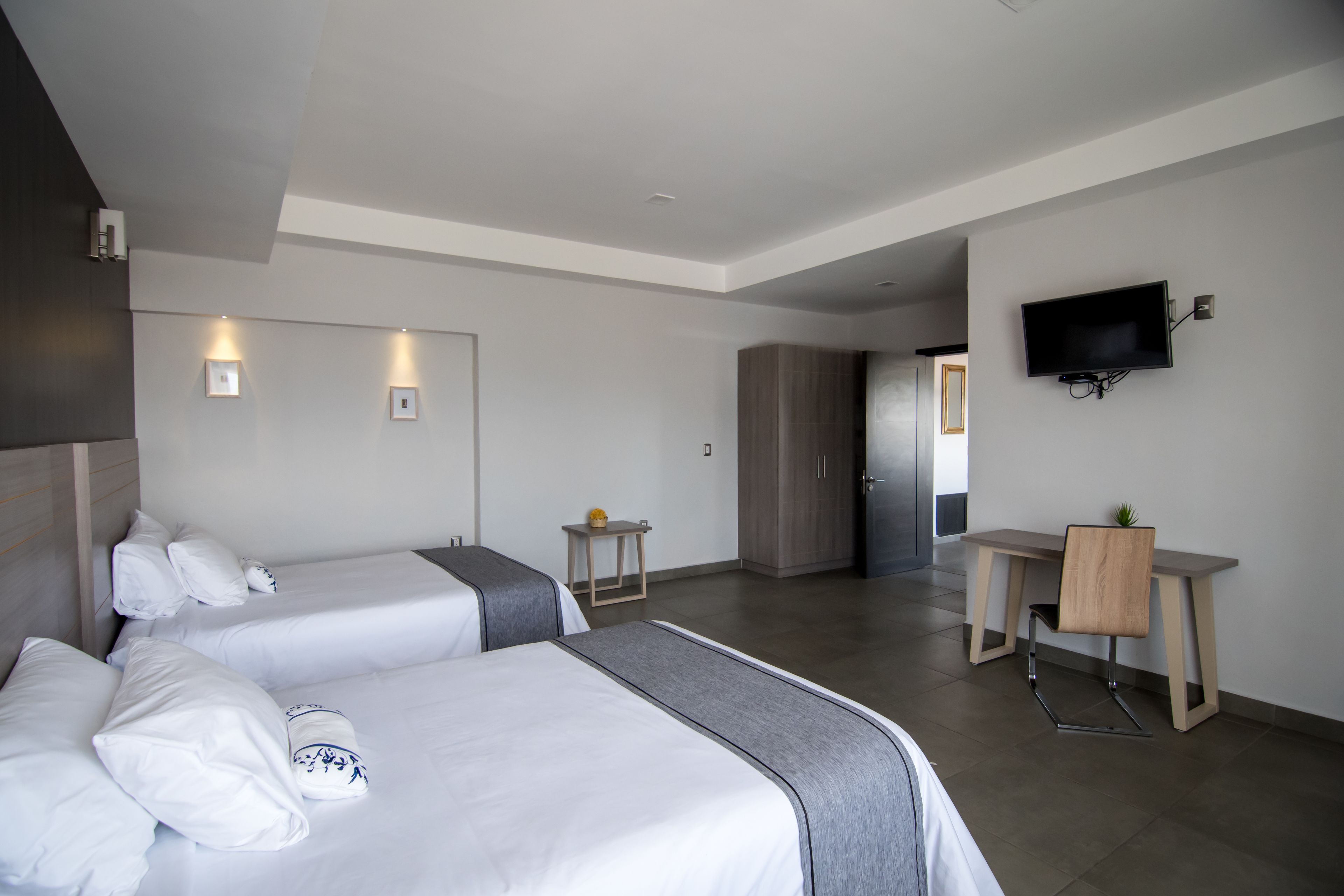 Une chambre d’hôtel avec deux lits, un bureau, une chaise, un téléviseur fixé au mur et une armoire.