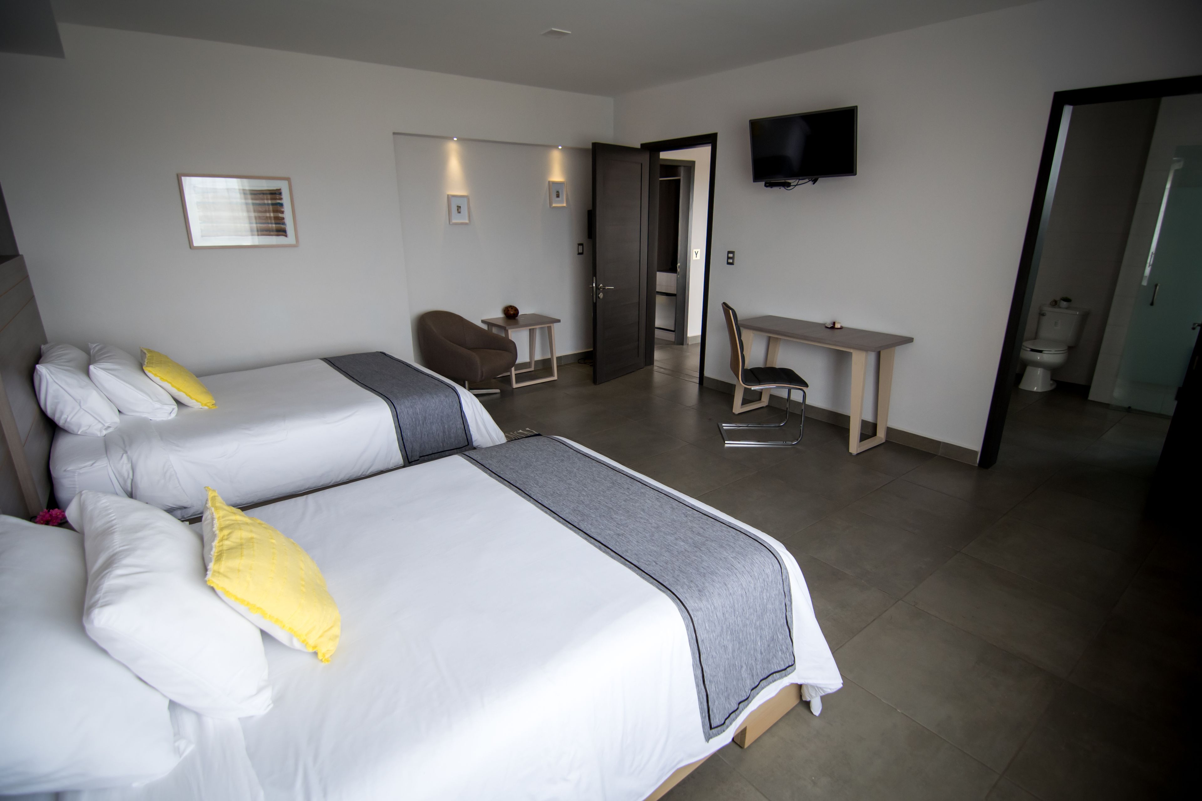 Ein Hotelzimmer mit zwei Betten, einem Schreibtisch, einem Sessel, einem Fernseher und einem durchgegangenen Badezimmer.