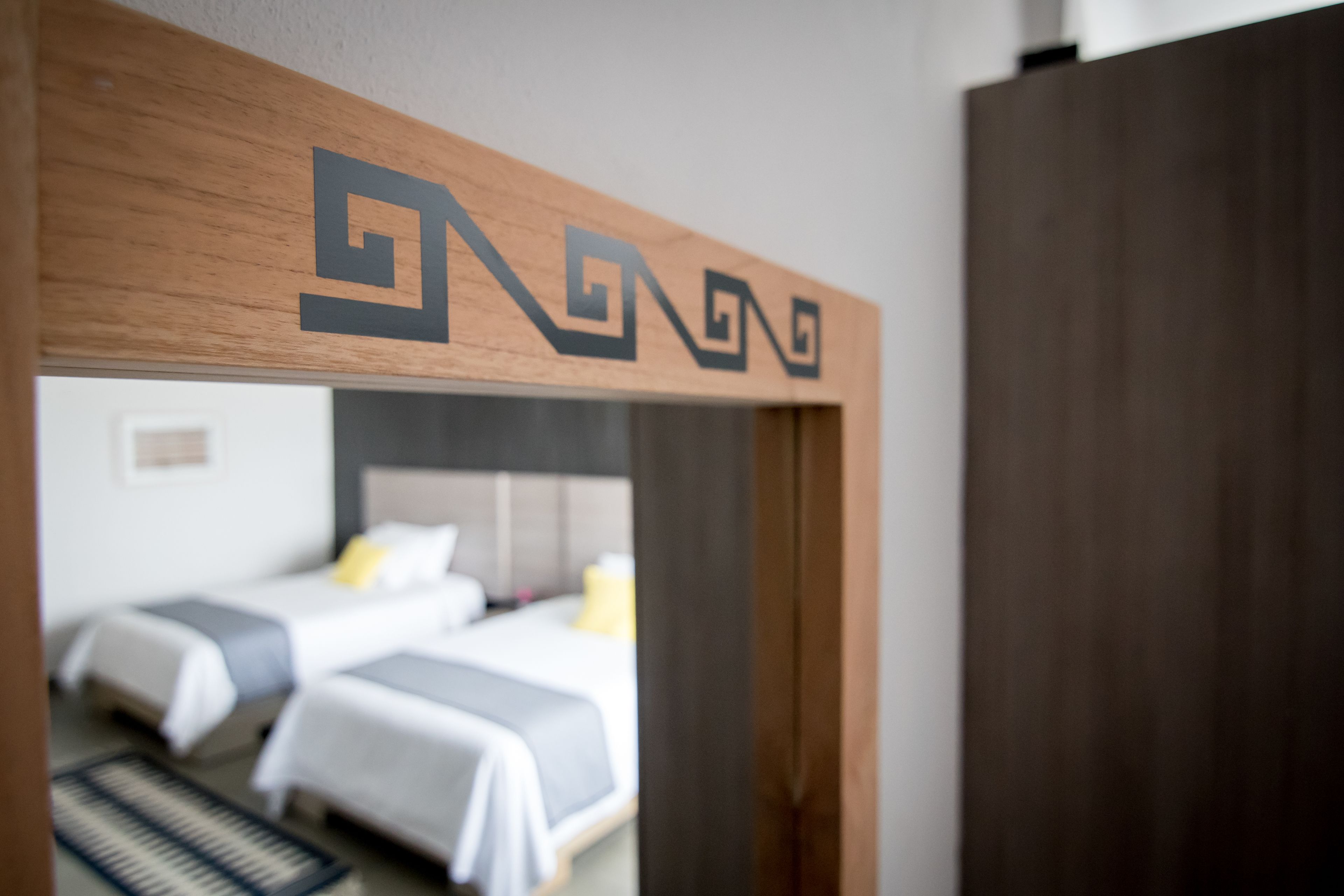 A doorway with a wooden frame and a logo, leading to a room with two beds and a headboard.