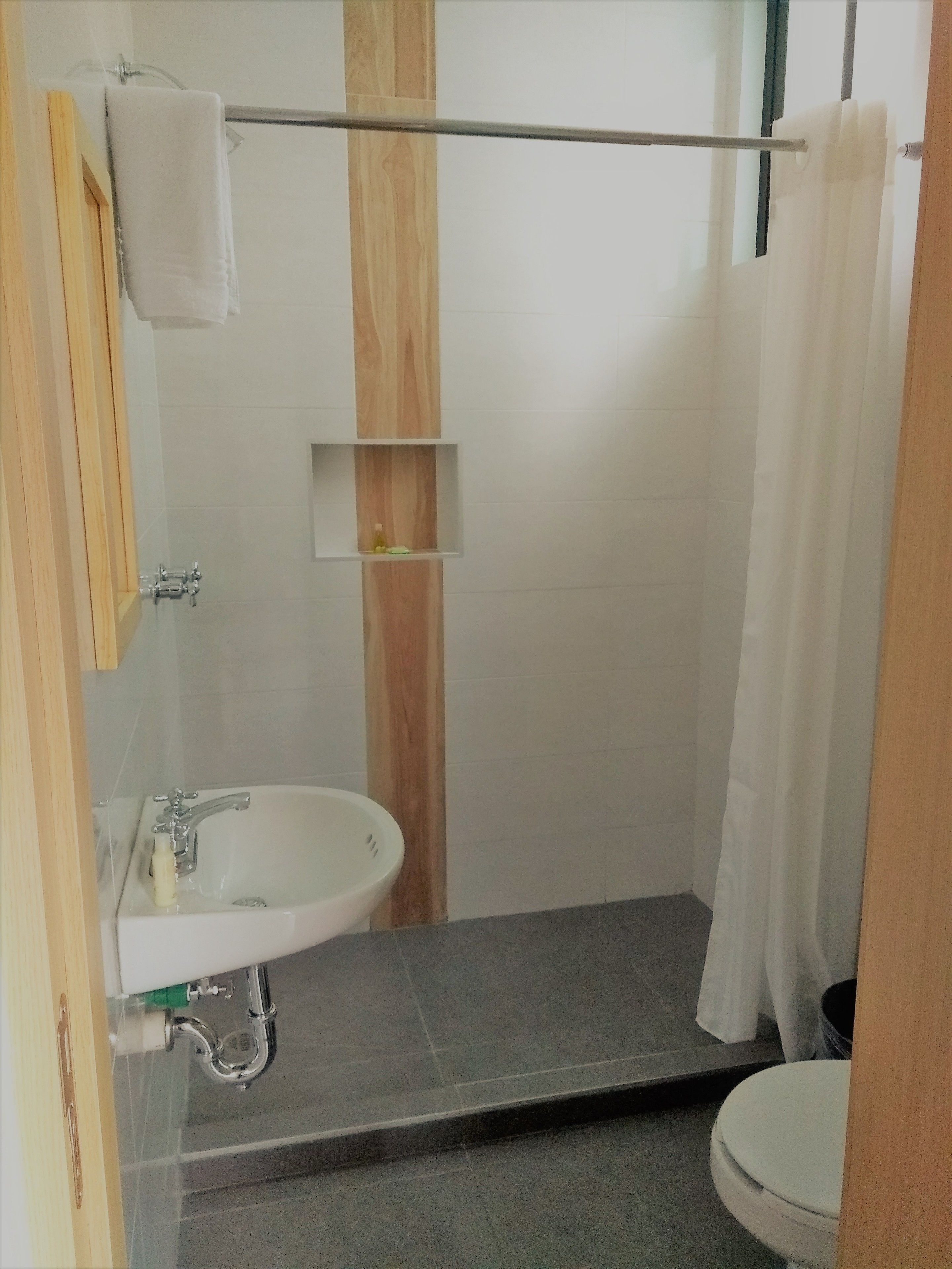 Un baño con un lavamanos blanco, un espejo, un perchero para toallas, una cortina de ducha y un inodoro.