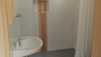 Un baño con un lavamanos blanco, un espejo, un perchero para toallas, una cortina de ducha y un inodoro.