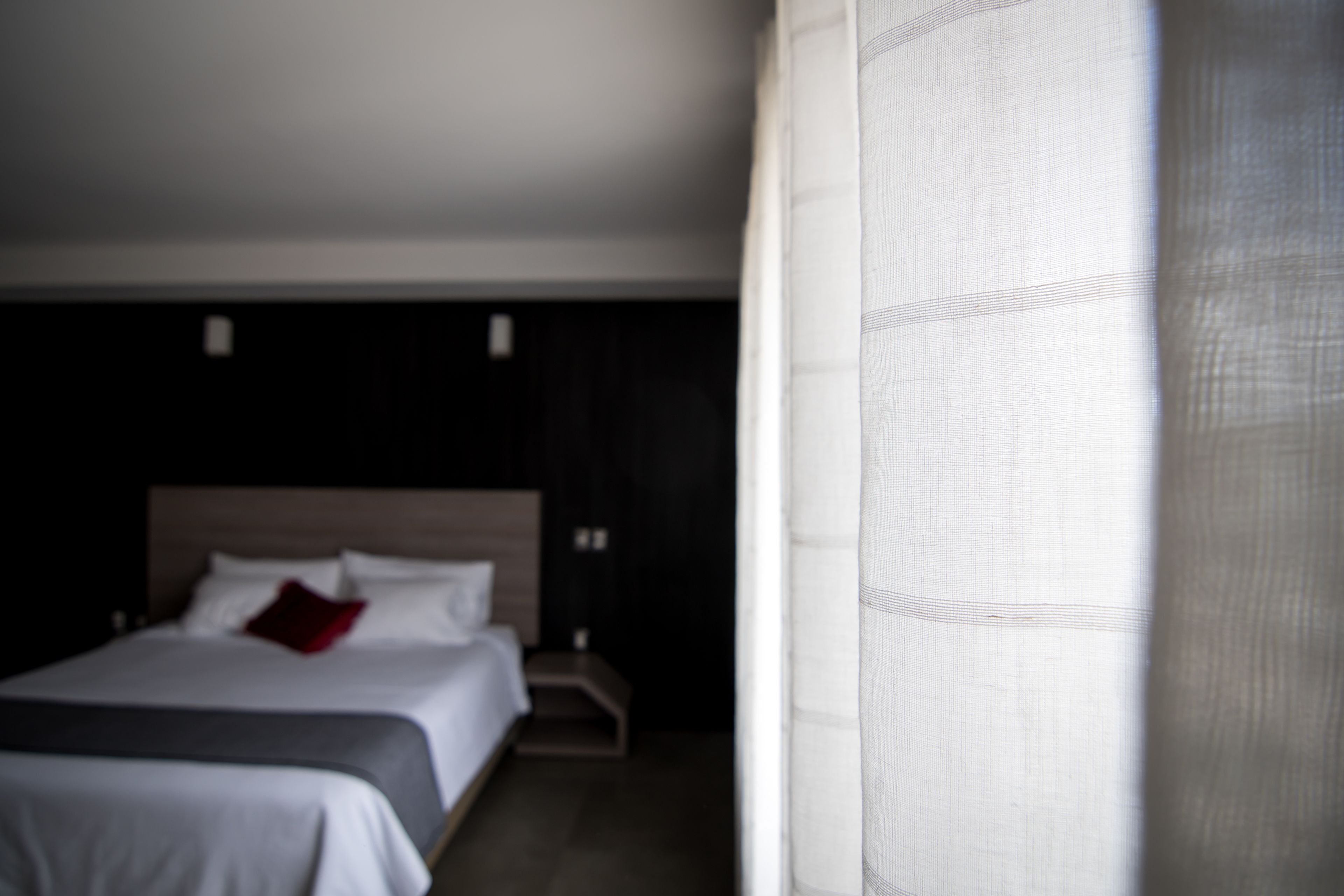 A hotel room with a bed, a nightstand, and a window with curtains.