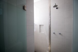 Un baño moderno con azulejos blancos, cabina de ducha de vidrio y panel de control a la vista.