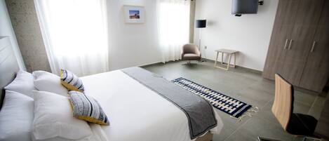 A modern hotel room with a large bed, a flat-screen TV mounted on the wall, a wardrobe, and a small table.