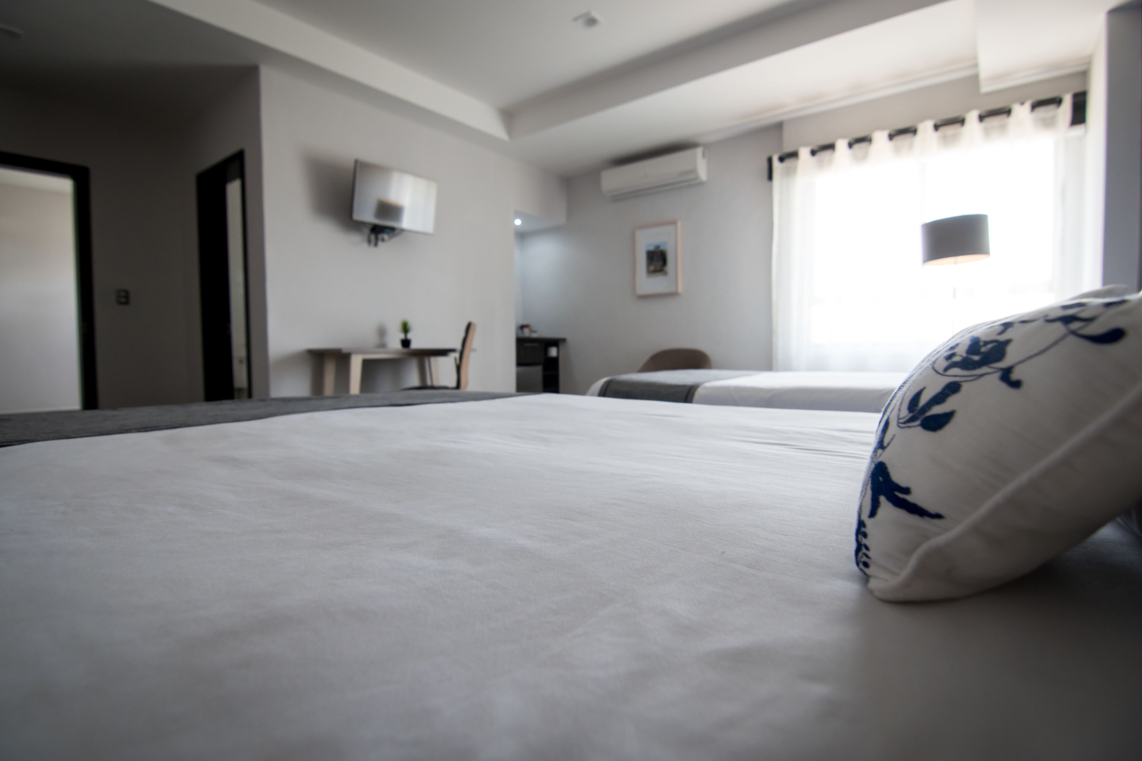 Habitación de hotel con una cama grande, un escritorio, una silla, un televisor montado en la pared y una ventana con cortinas.