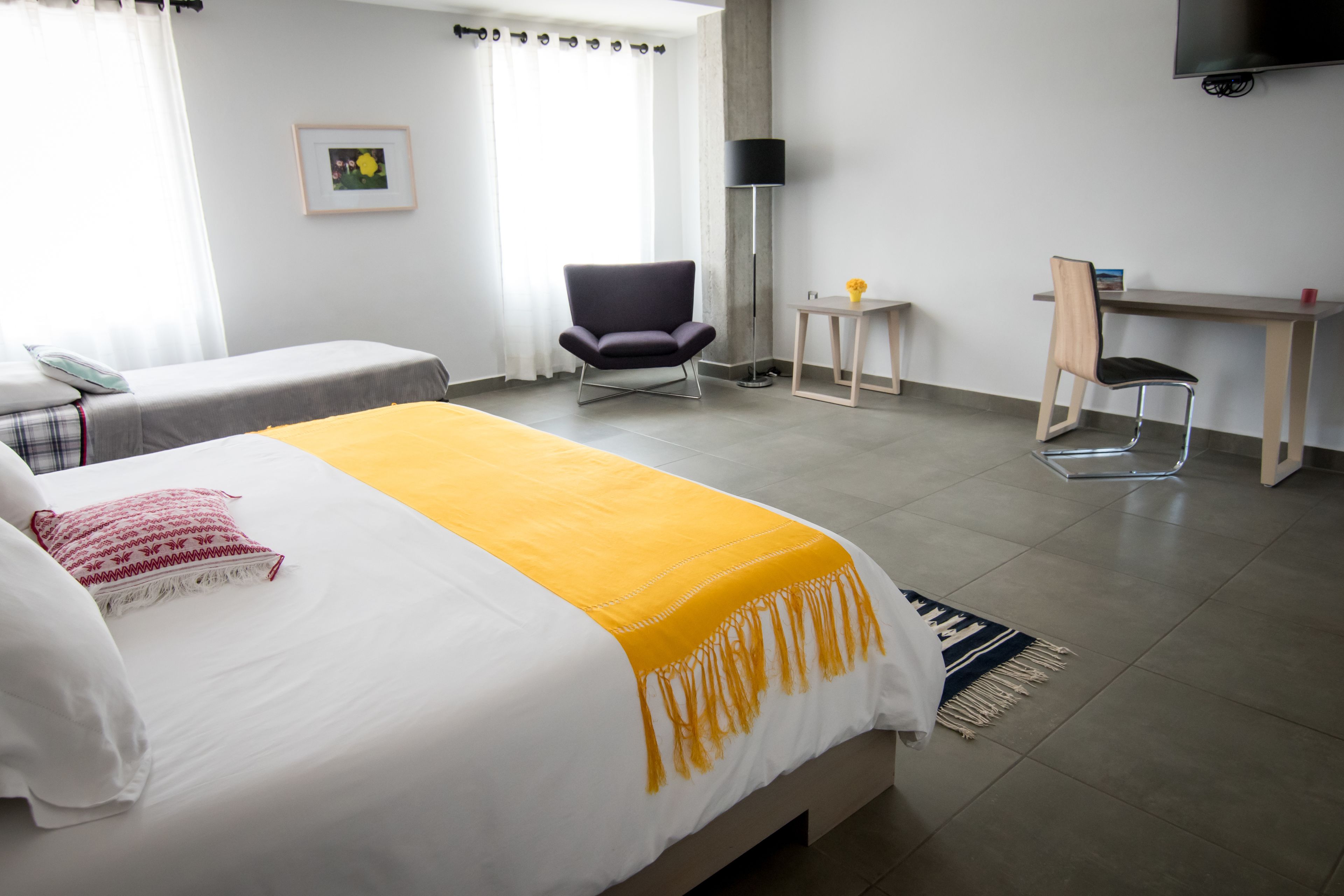 Une chambre d’hôtel avec un lit, deux chaises, un bureau, une télévision et une petite table sur laquelle se trouve un vase.