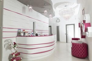 Un'area reception con un bancone bianco curvo, dettagli rosa, un lampadario e una zona salotto imbottita rosa.