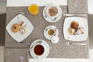 Colazione con diversi pasticcini, un bicchiere di succo d'arancia e una tazza di tè su un sottopiattino decorato.