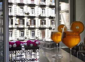 Twee glazen drankje met een schijfje sinaasappel op de rand, geplaatst op een balkon met uitzicht op een gebouw met balkons en een bloemstuk.