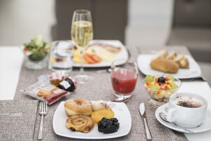 Una mesa servida con diversos productos para el desayuno, incluyendo bollería, un cuenco de fruta, un vaso de jugo de uva y una taza de café.