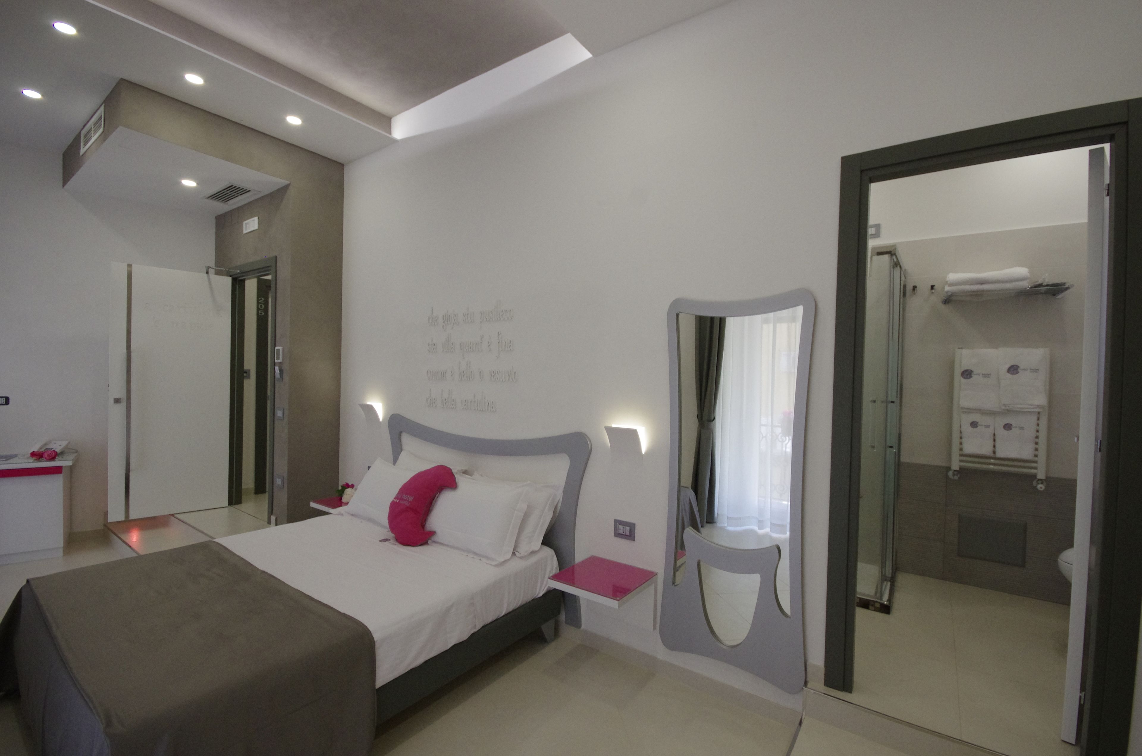 Ein modernes Hotelzimmer mit Bett, Nachttisch und einem durchgegangenen Tür sichtbaren Badezimmer.