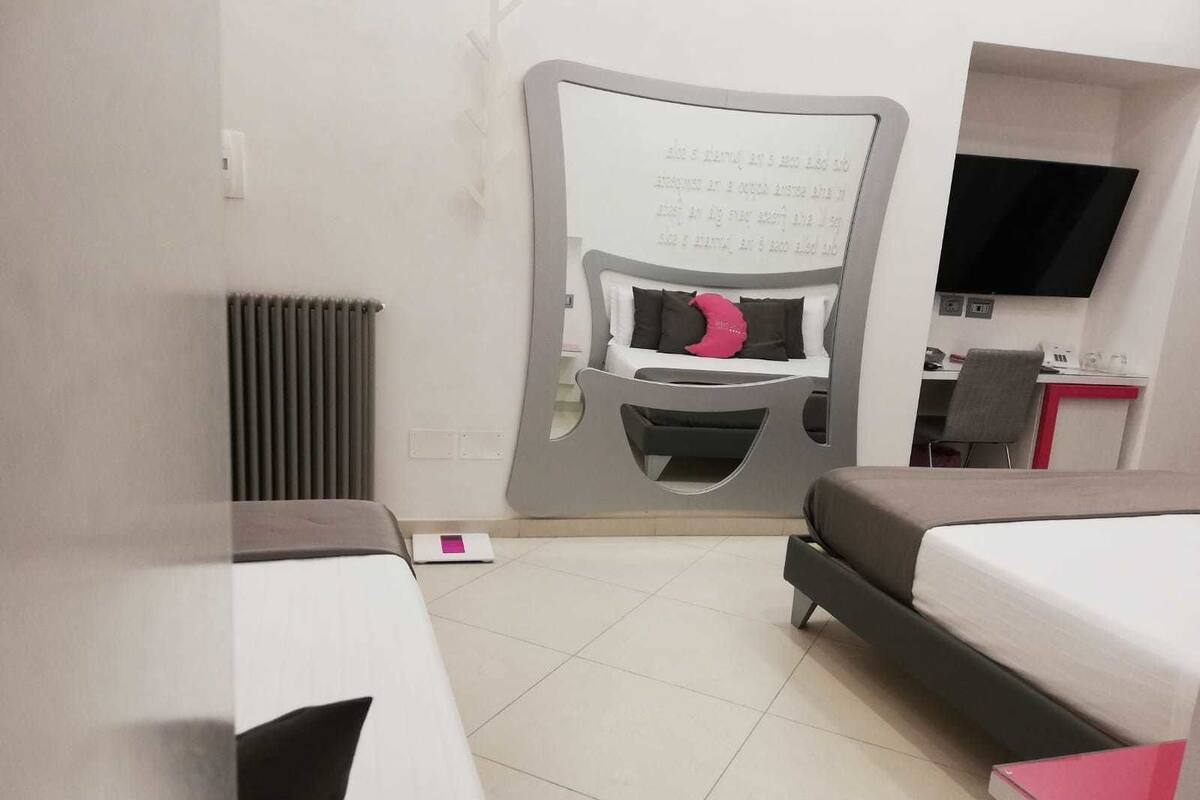 Une chambre d’hôtel moderne avec un grand lit, un bureau et une chaise. Il y a un radiateur au mur et un téléviseur fixé au mur.