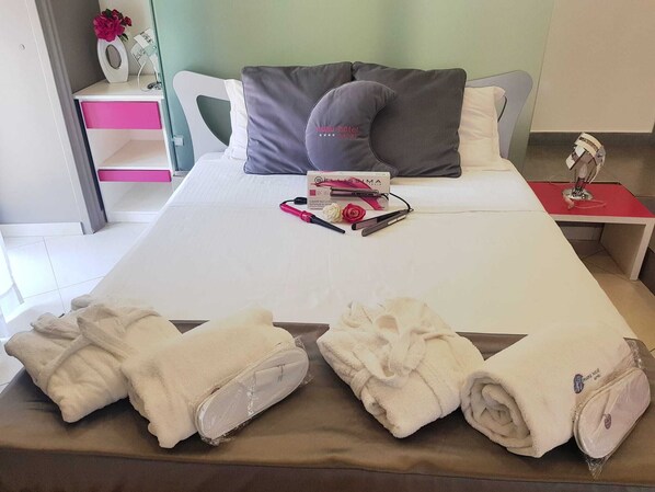 A neatly made bed with pillows, a bedside table with a lamp, and a small desk with a vase of flowers.