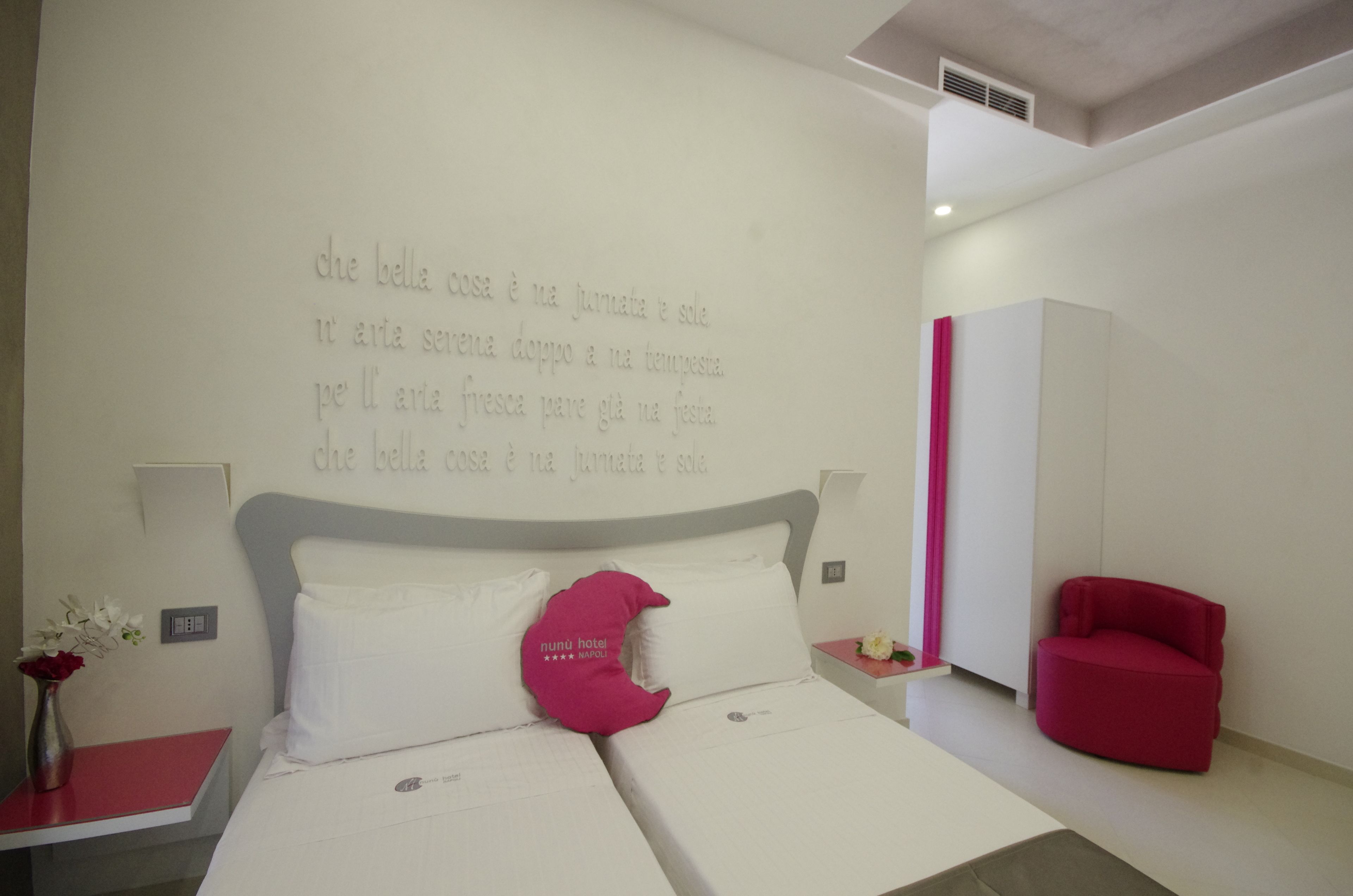 Una camera d'albergo con un letto, un comodino, una poltrona rossa e una parete con scritte.