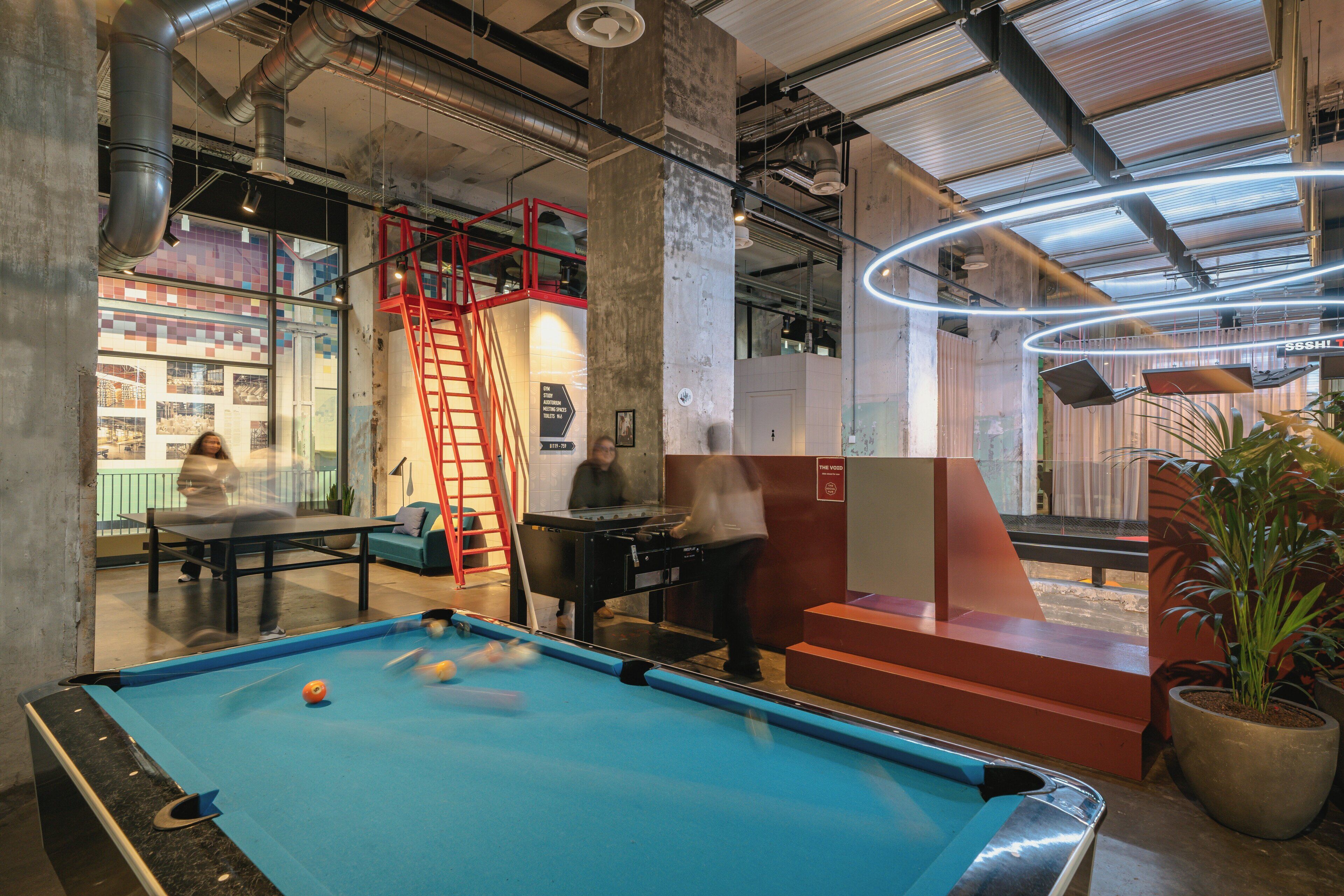 A pool table in a modern indoor space with visible structural elements and a red ladder.