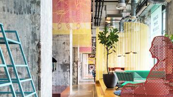 A modern interior with exposed ductwork, a concrete wall, a yellow reception desk, a red perforated chair, and a large banner with text.