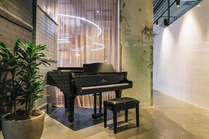 A grand piano in a hallway with a potted plant and a bench. - The Social Hub Maastricht (Maastricht)