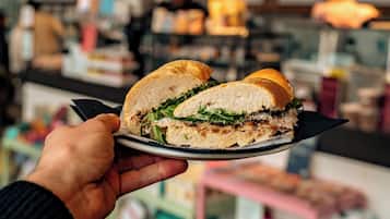 A sandwich being held over a plate, with a blurred background of a cafe or restaurant.