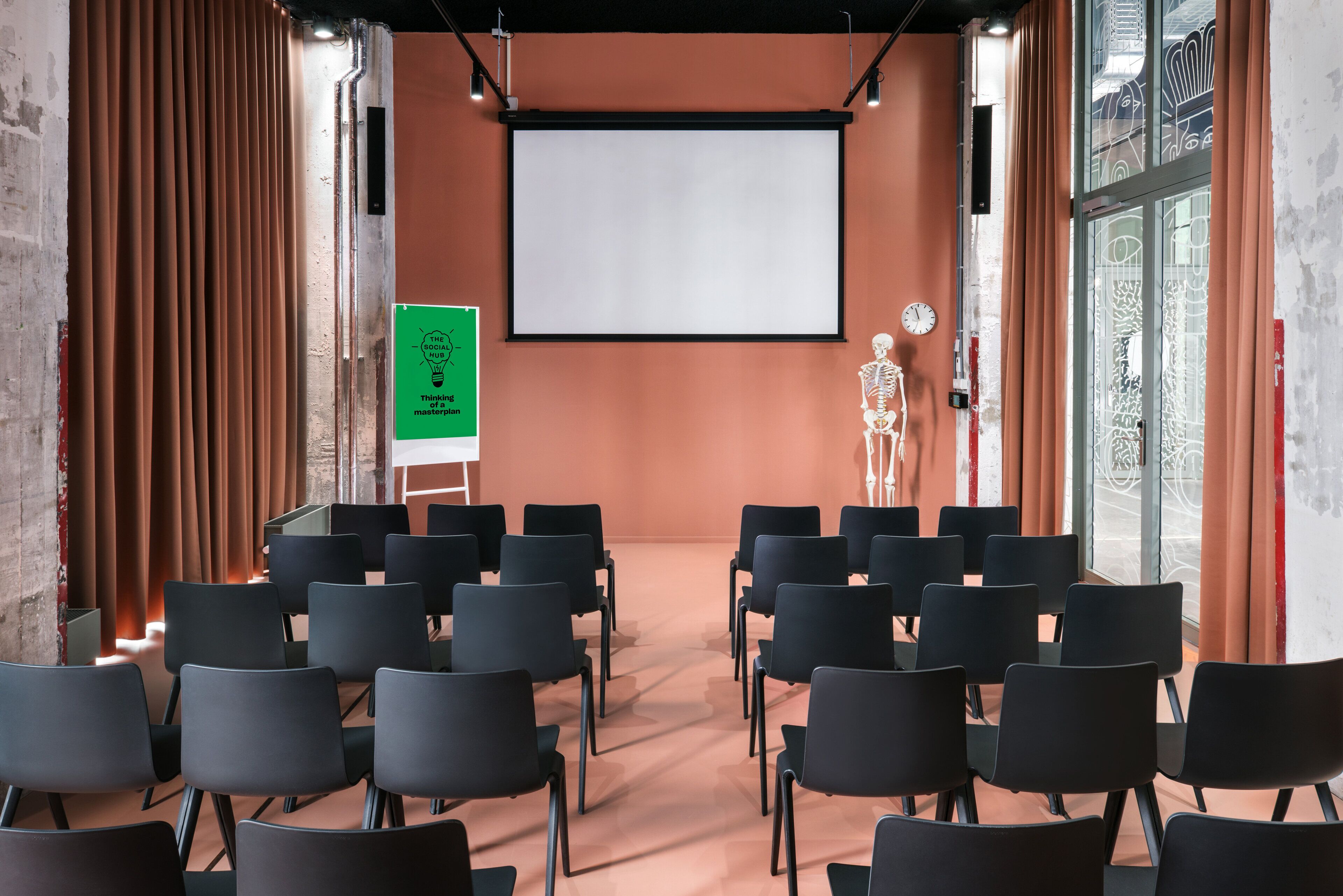Een vergaderzaal met een groot scherm, zwarte stoelen en een skelet decoratie.