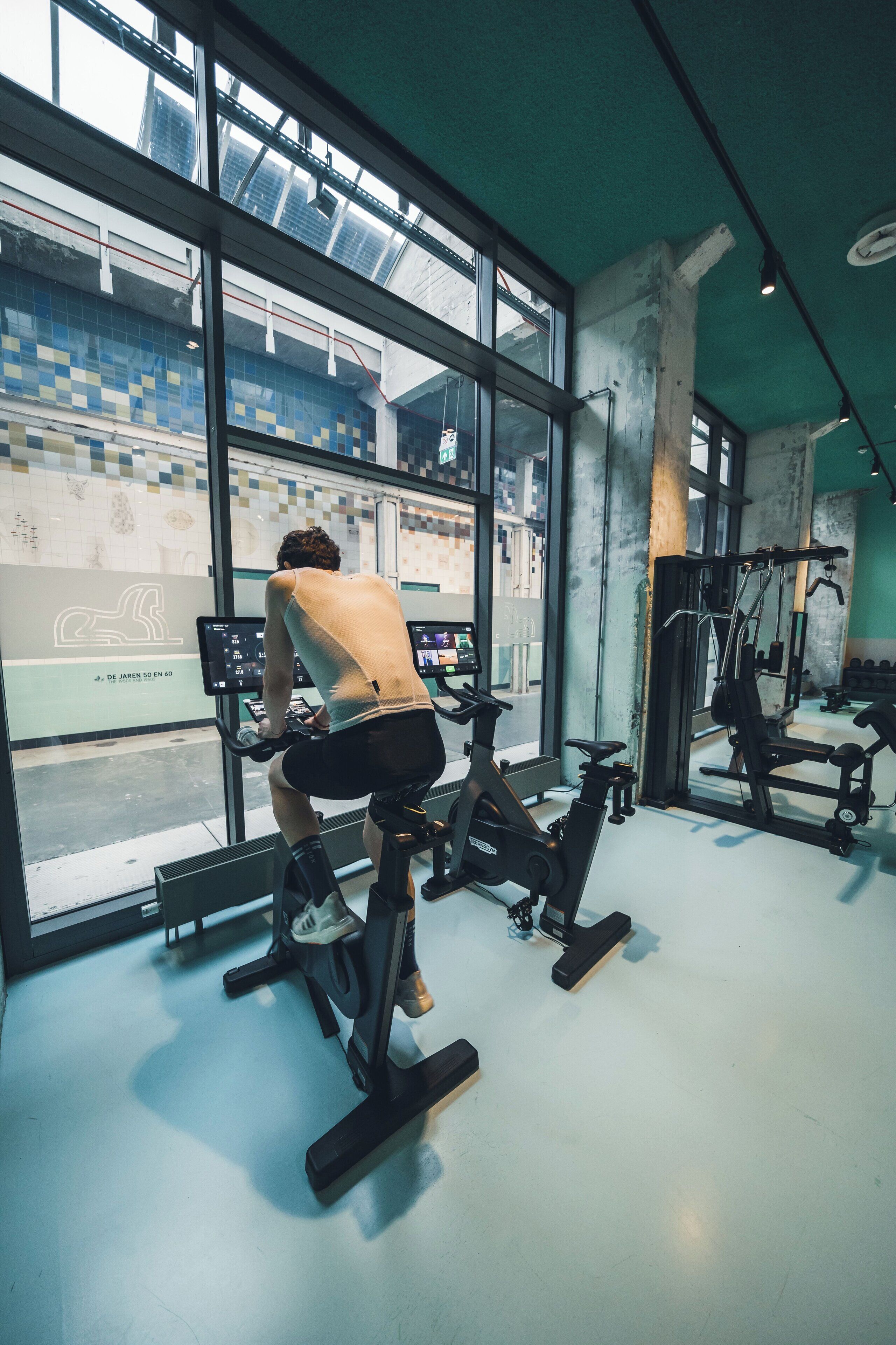 A gym with exercise bikes, a mirrored wall, and large windows overlooking a cityscape.