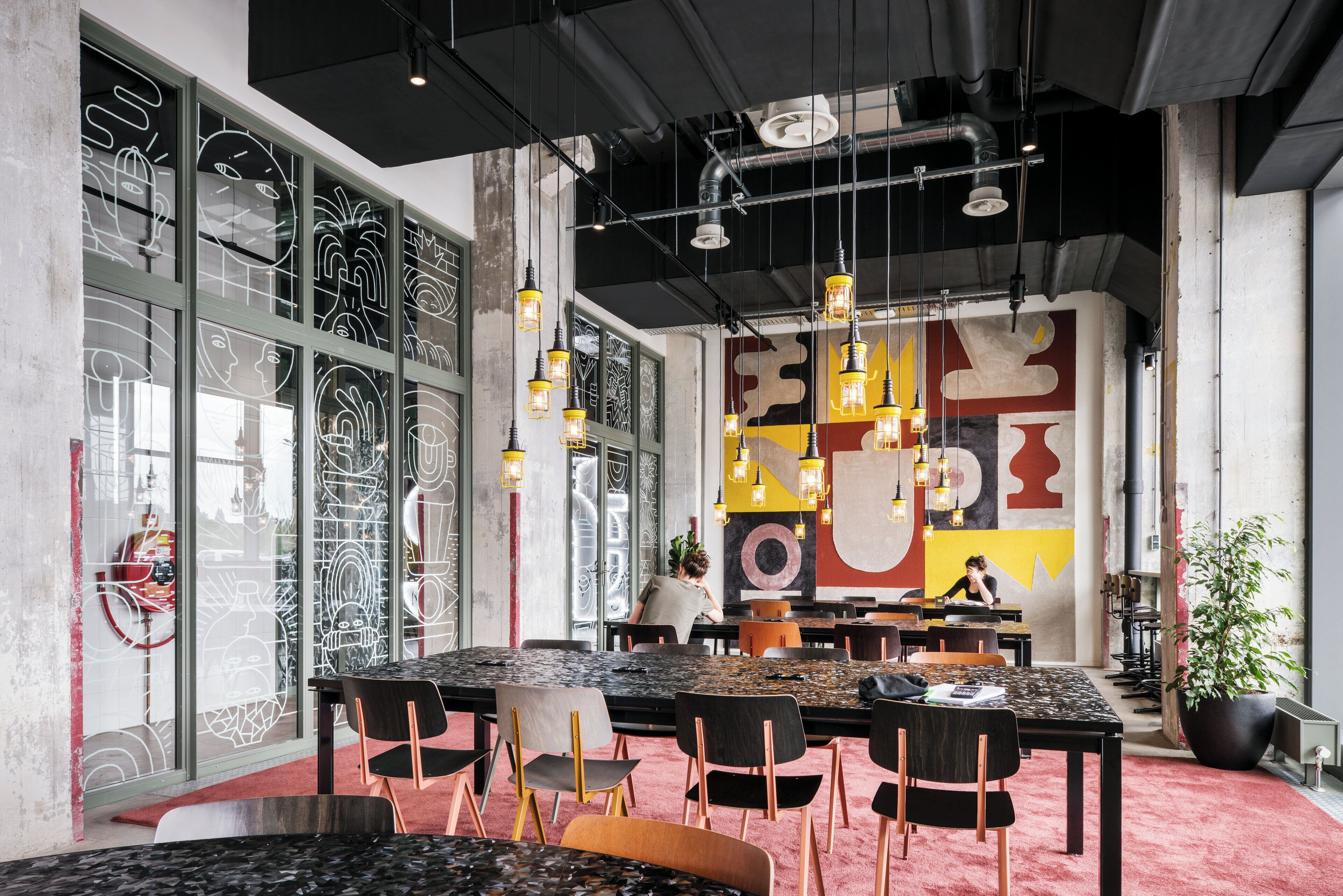 Un comedor moderno con una mesa grande, sillas, lámparas colgantes y un mural en la pared.