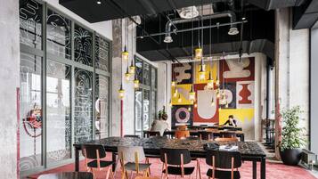 Un comedor moderno con una mesa grande, sillas, lámparas colgantes y un mural en la pared.