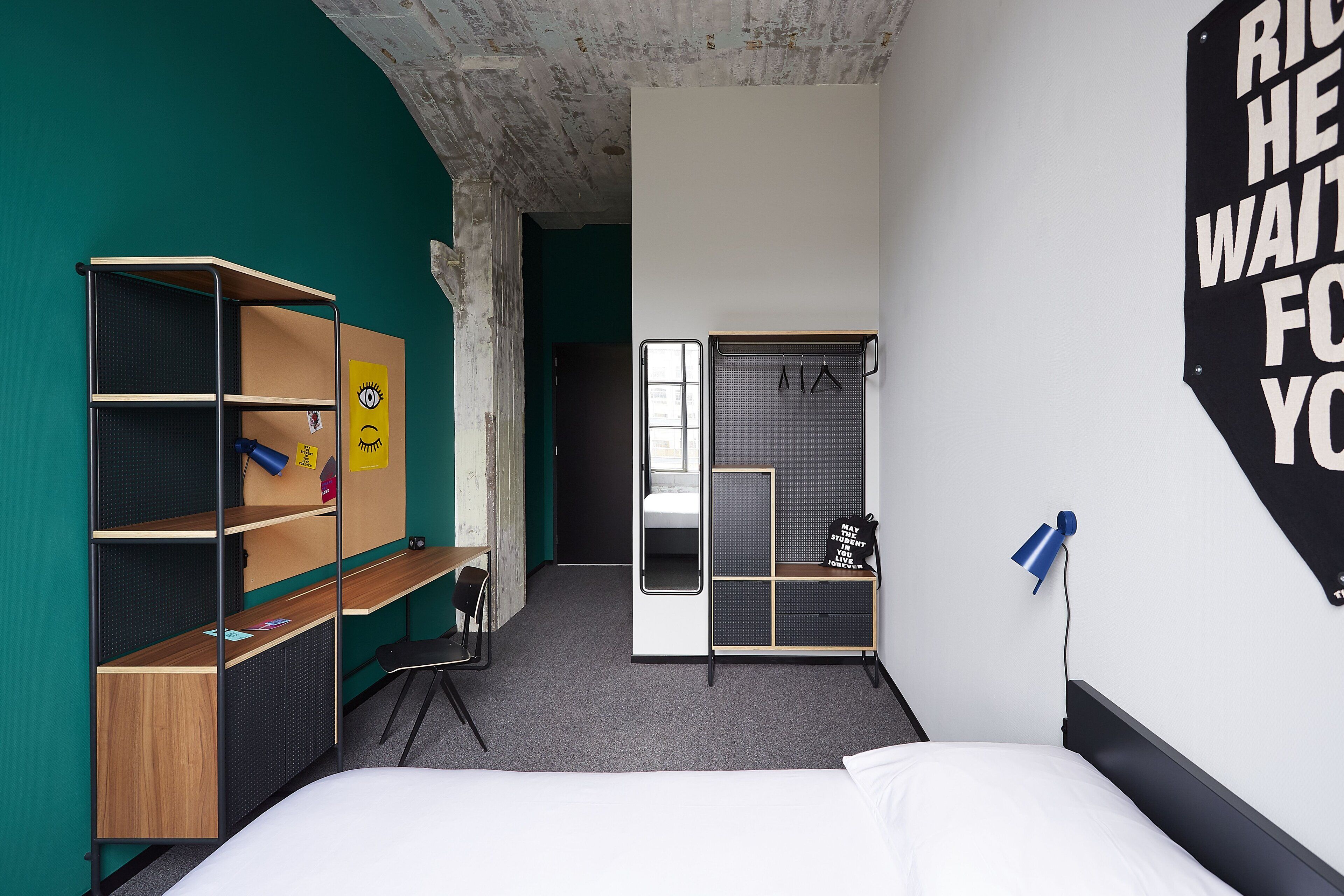 A compact hotel room with a bunk bed, a desk with a chair, a wardrobe, and a large mirror.