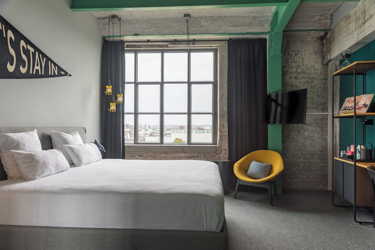 Una habitación de hotel con una cama grande, una silla amarilla, un televisor y una estantería.