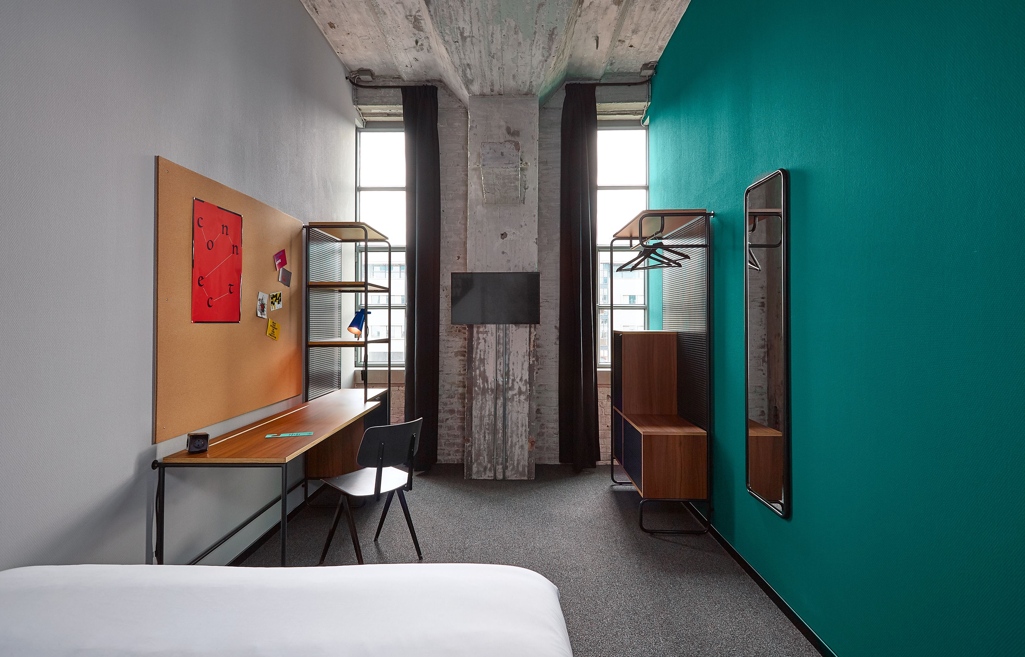 A hotel room with a bed, a desk, a chair, a TV, a wardrobe, and a large window.